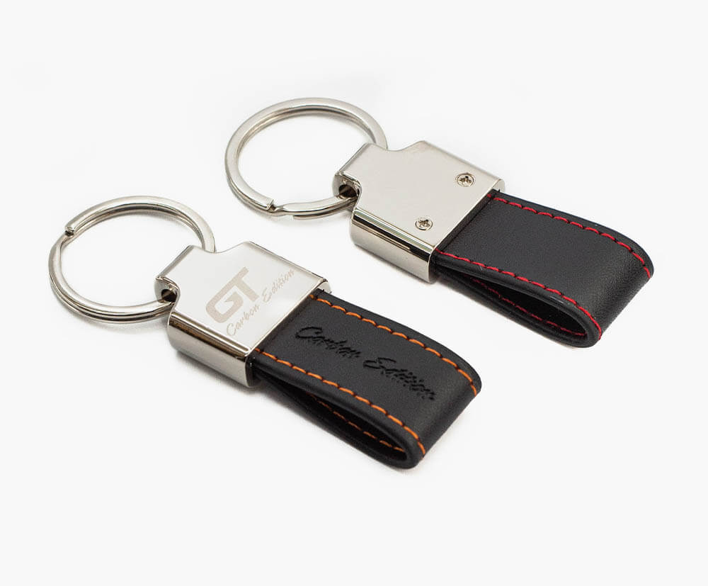 Promotional keyring with embossed mini PU leather strap, coloured stitching and engraved metal attachment.